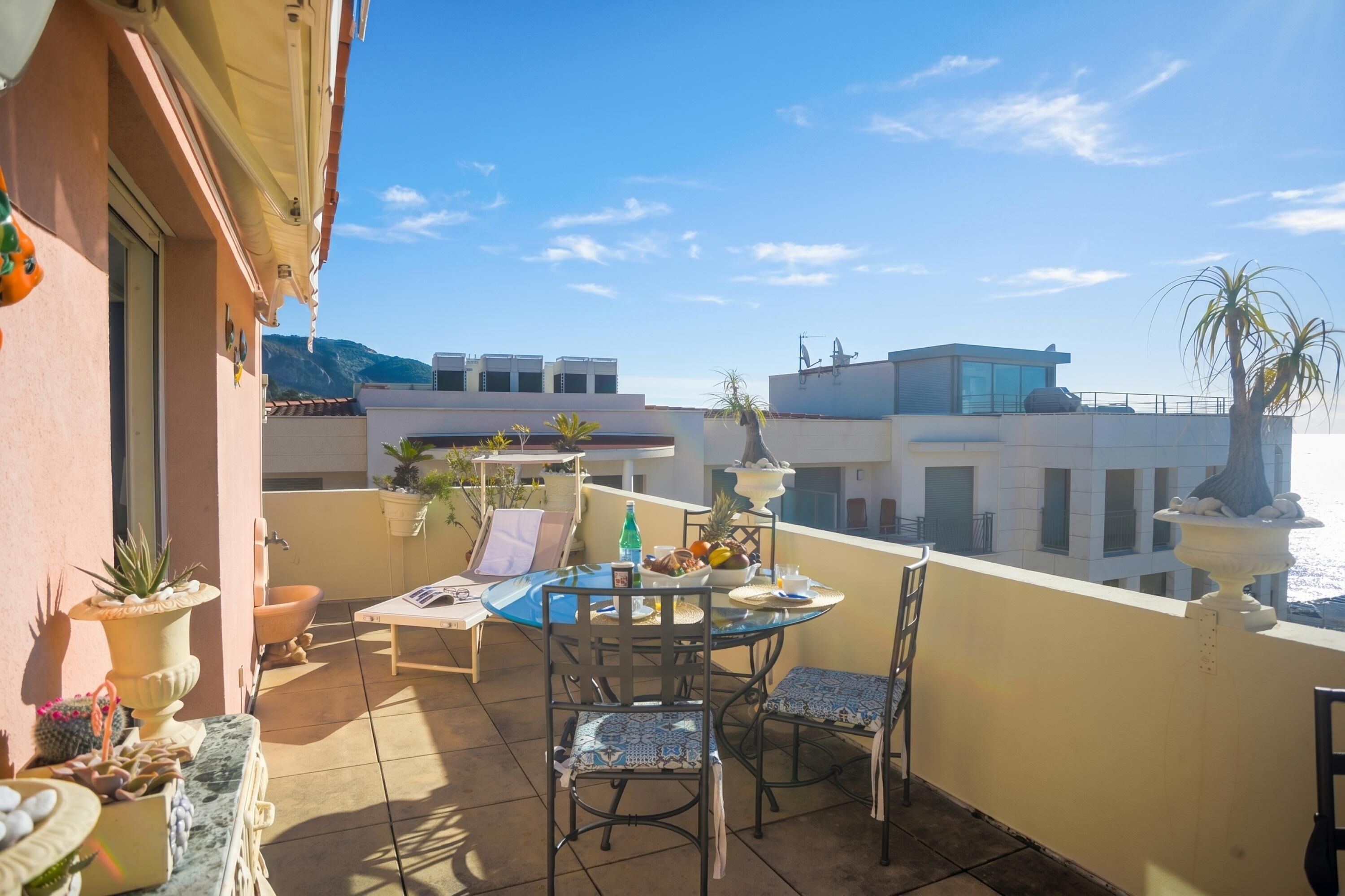 A balcony with a table set for dining, potted plants, and a view of surrounding buildings.