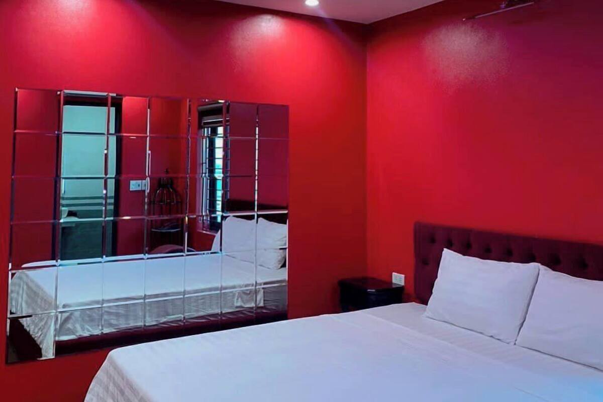 A hotel room with a large bed, a mirror, and red walls.