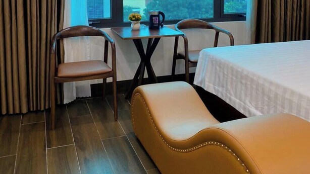 A hotel room with a bed, a sofa, a table with chairs, and a large window offering a city view. - Thuong Hai Hotel - by Bay Luxury (Hanoi)