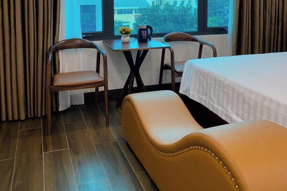 A hotel room with a bed, a sofa, a table with chairs, and a large window offering a city view.
