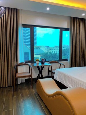 Habitación de hotel con cama, sofá, mesa y sillas, y un ventanal con vistas a la ciudad.