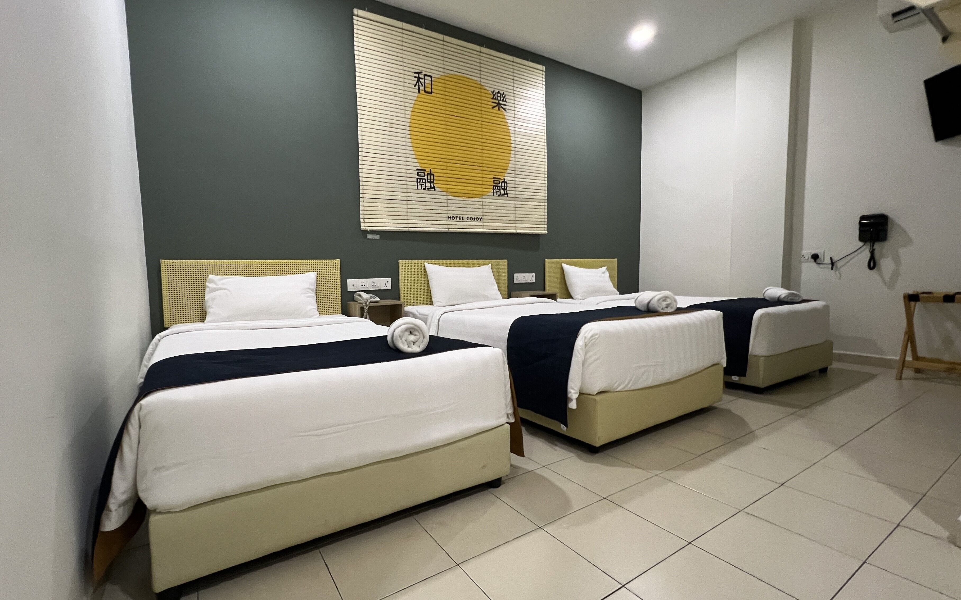 A hotel room with two beds, a large window with blinds, a wall-mounted phone, and a small table.