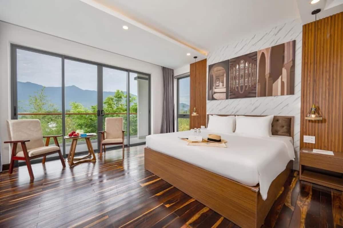 A modern hotel room with a large bed, wooden flooring, and a balcony with a mountain view.
