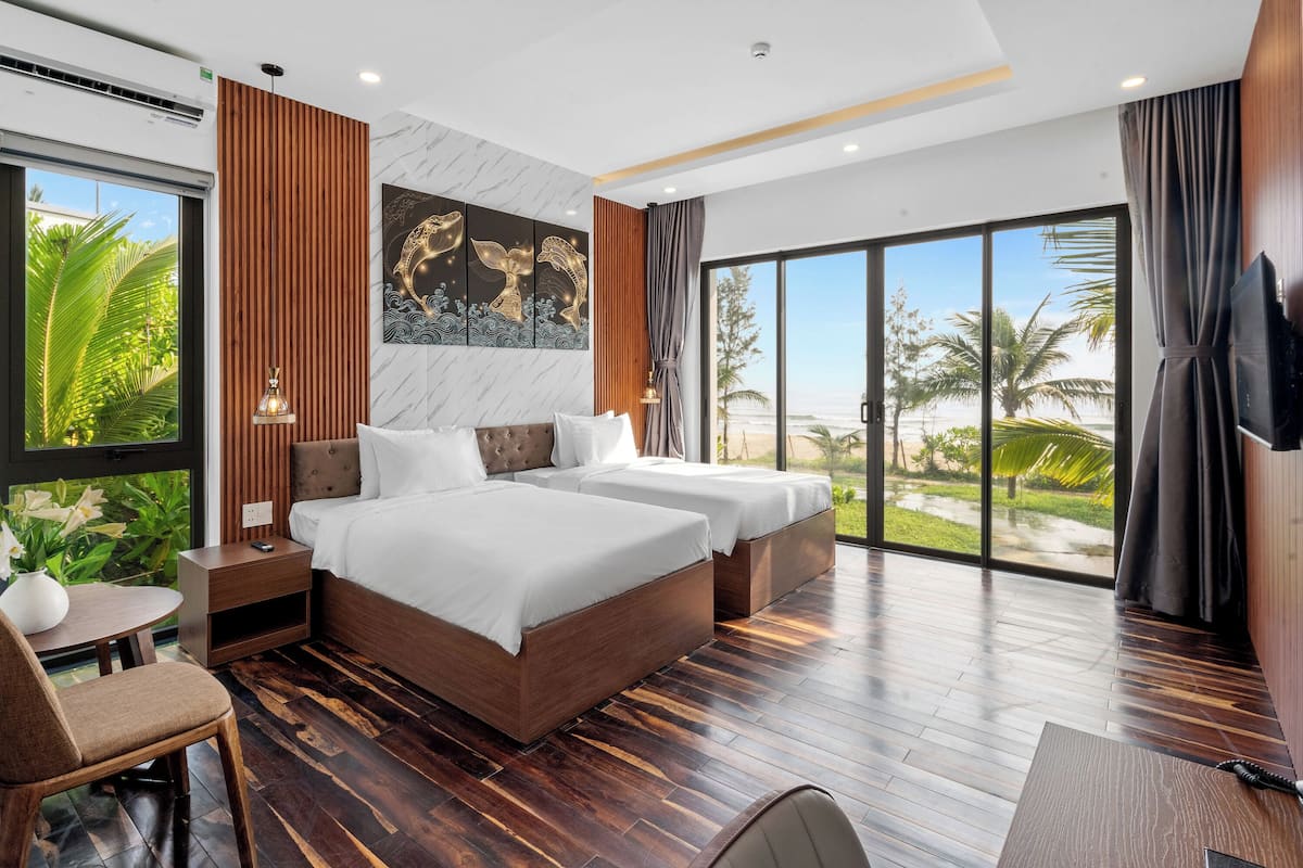 A modern hotel room with a large bed, a desk, and a view of the beach.