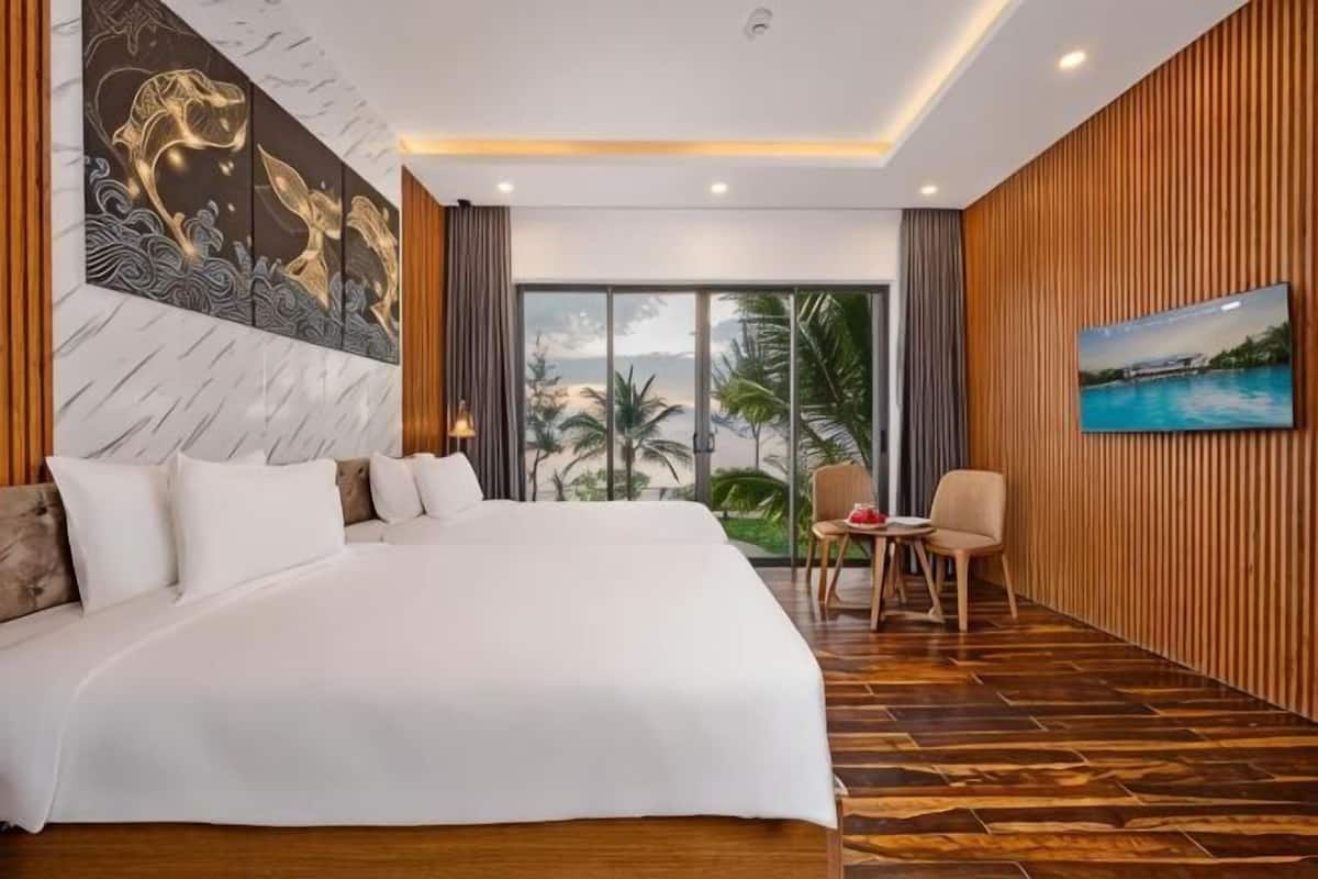 A hotel room with a large bed, a desk with a chair, a view of palm trees, and a painting on the wall.