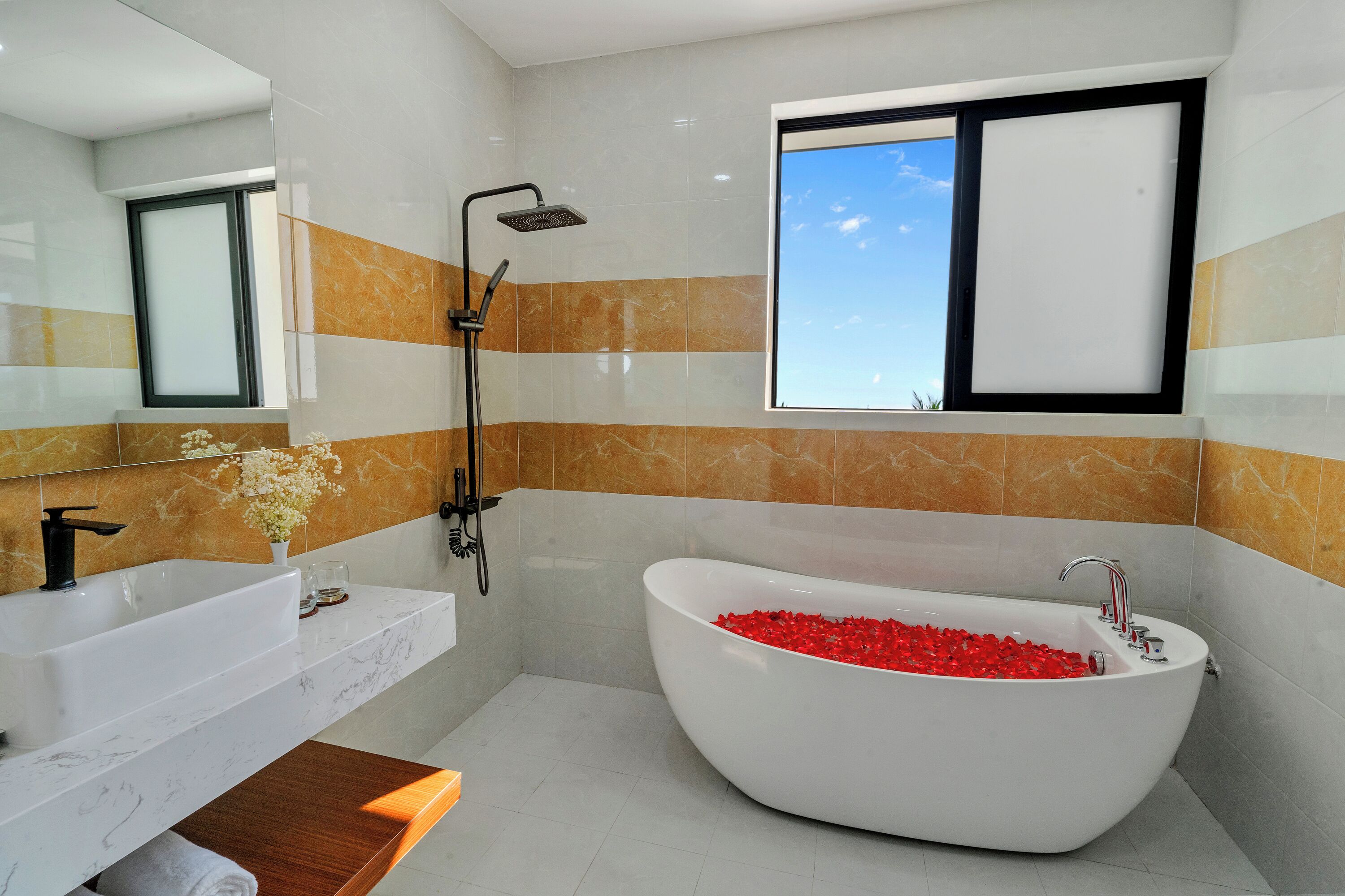 A modern bathroom with a large white bathtub filled with red bath items, a separate sink, and a shower.
