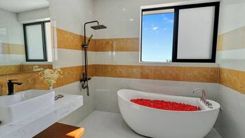 A modern bathroom with a large white bathtub filled with red bath items, a separate sink, and a shower.