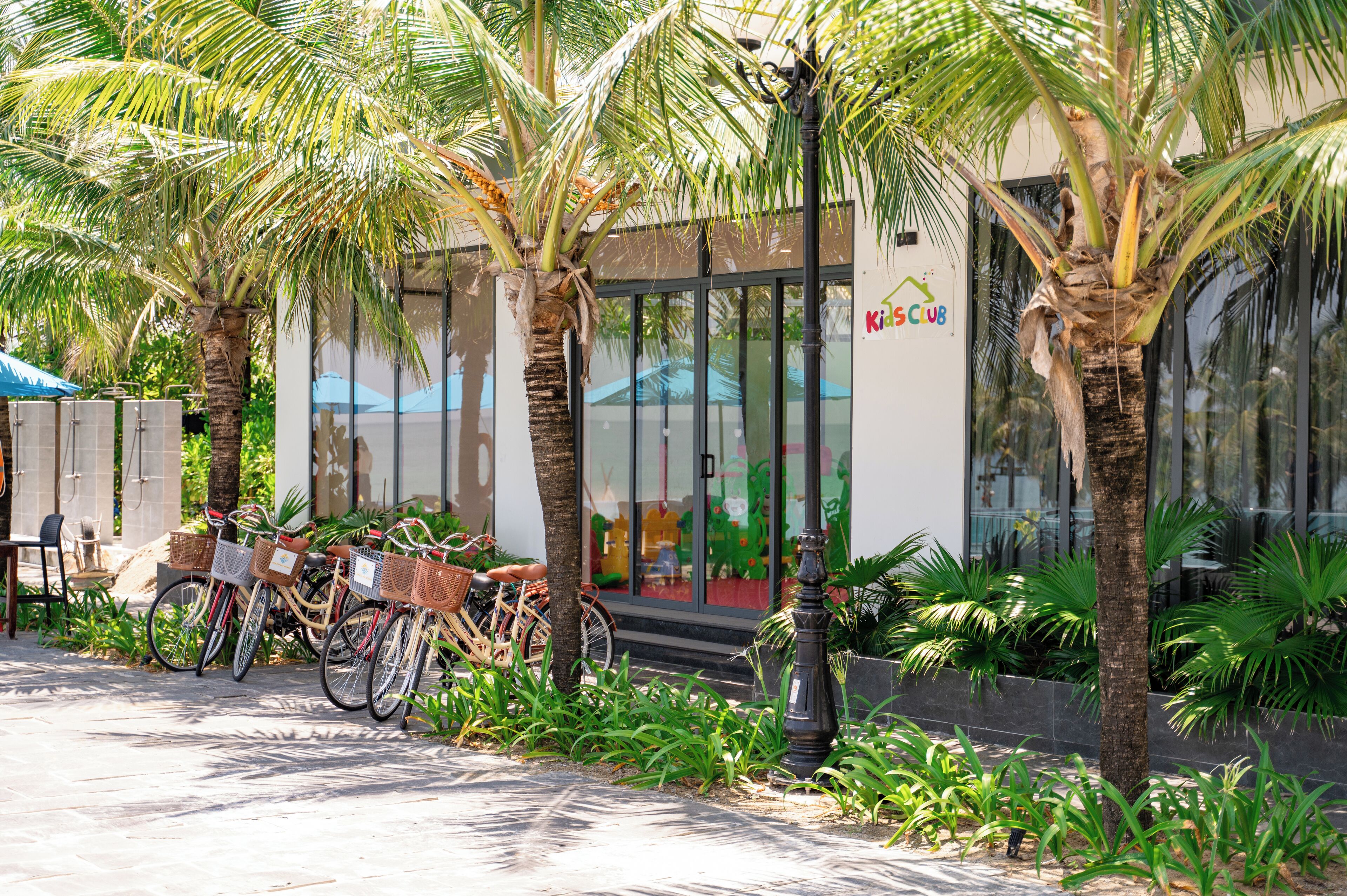 A building with a Kids Club sign, bicycles parked outside, and palm trees.
