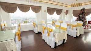 A banquet hall with round tables, white tablecloths, and chairs with gold sashes. - Hoa Hong 1 Hotel - by Bay Luxury (Hanoi)
