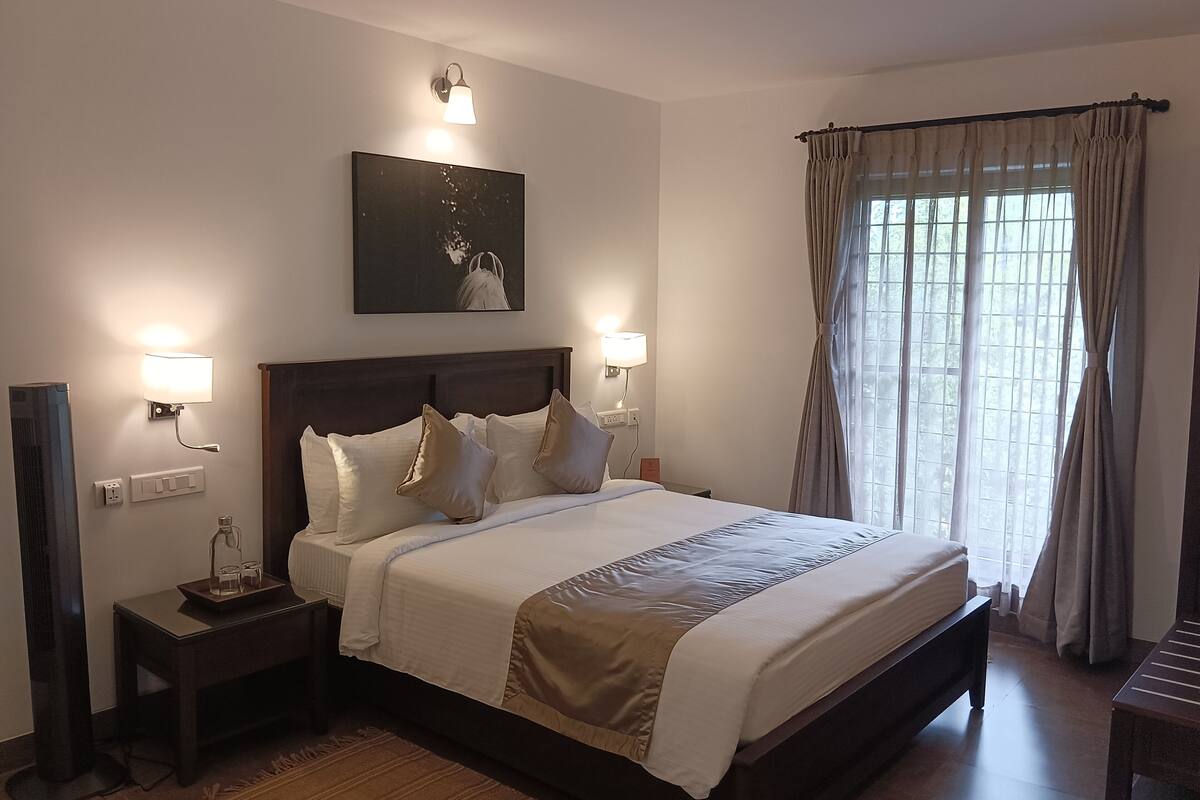 Uma cama bem arrumada com cabeceira, duas luminárias de cabeceira, uma mesinha de cabeceira com um copo e um quadro na parede.