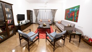 Una sala de estar con un sofá, dos sillones, una mesa de centro, una estantería, un televisor y un cuadro en la pared.