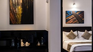 Habitación de hotel con cama, mesita de noche, cafetera y dos cuadros en la pared.