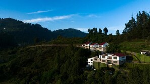A hillside property with multiple buildings, likely residential, surrounded by lush greenery and hills. - Dvara Luxury Resort Kodaikanal (Kodaikanal)