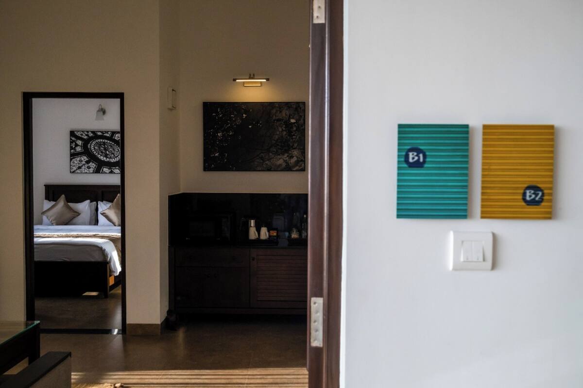 Quarto de hotel com uma cama, penteadeira, um quadro e uma parede com dois sinais numerados.