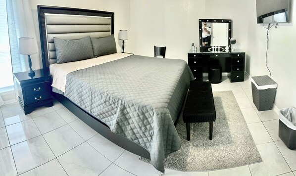 Quarto bem arrumado com cama, mesas de cabeceira, toucador com espelho e lixeira.