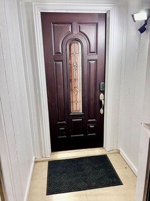Una puerta de madera oscura con un panel de vidrio decorativo y una cerradura con teclado, además de un felpudo.