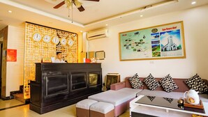 A hotel reception area with a reception desk, a sofa with patterned cushions, a coffee table, and a wall map. - Sapa Crown Hotel (Sa Pa)