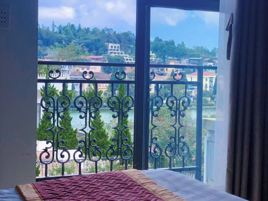 Una habitación con un amplio ventanal que da a un balcón con barandilla de hierro forjado y vistas a edificios y árboles.