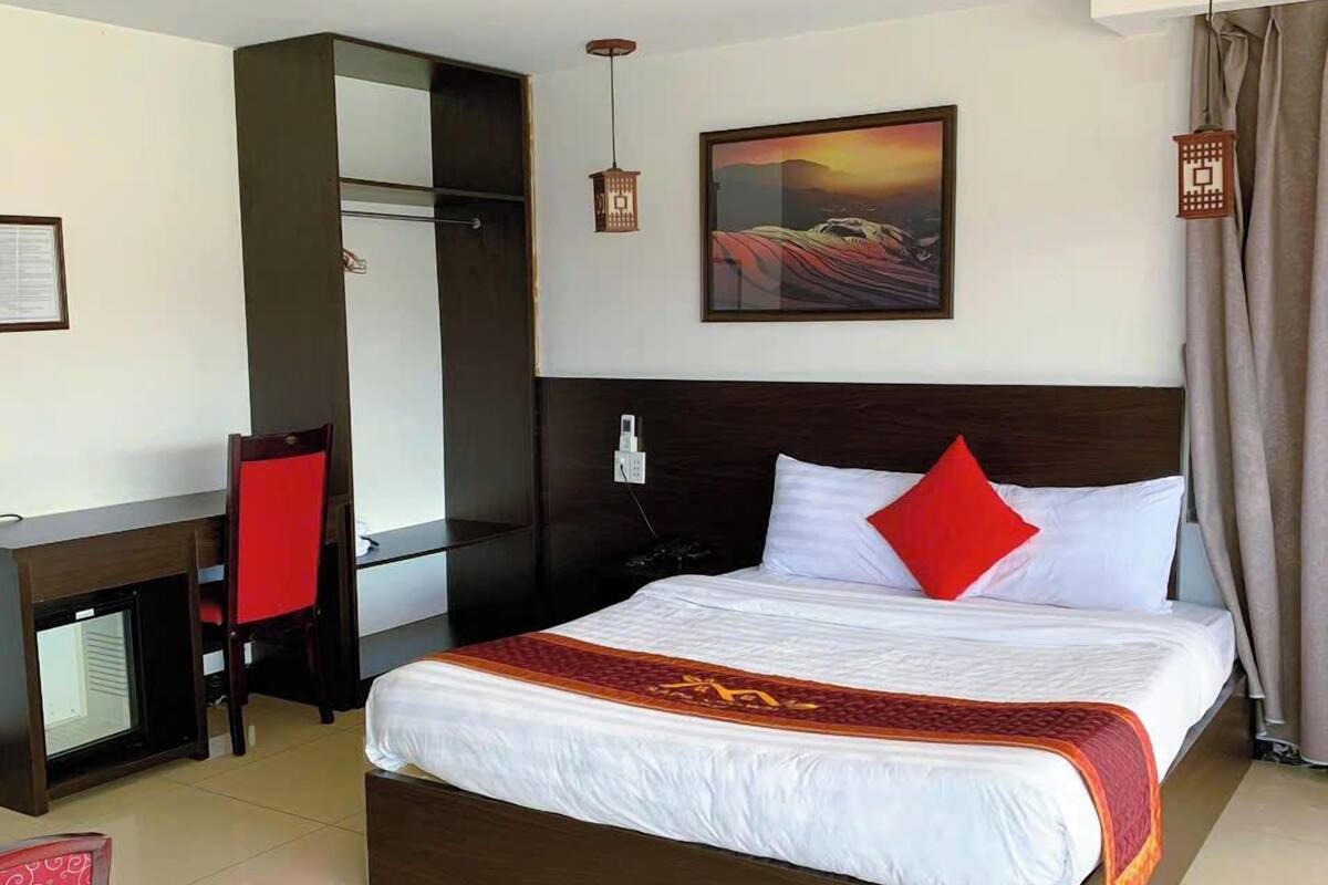 Quarto de hotel com cama, escrivaninha, cadeira, guarda-roupa e um quadro na parede.