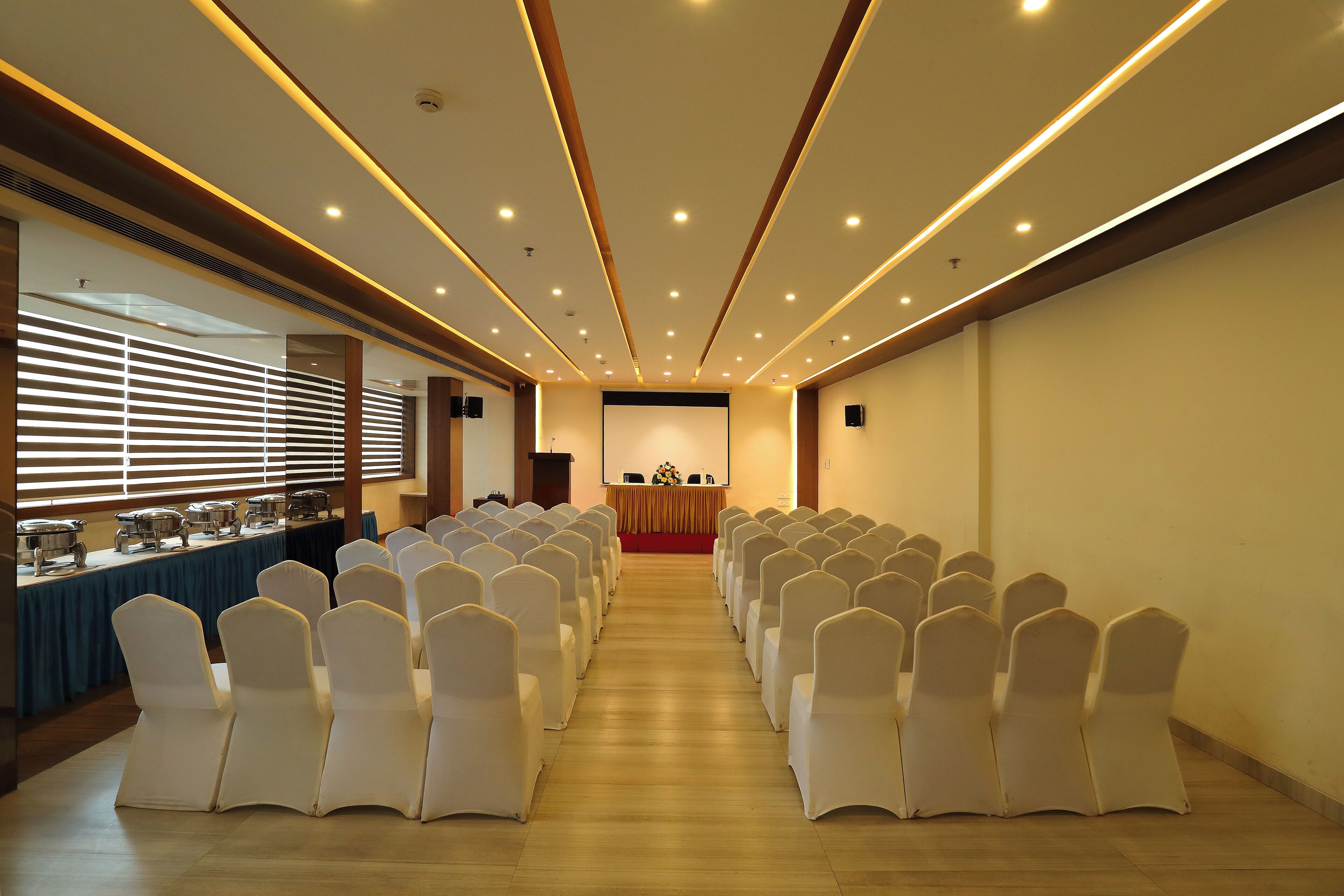 A conference room with rows of white chairs, a buffet table, and a podium at the front.