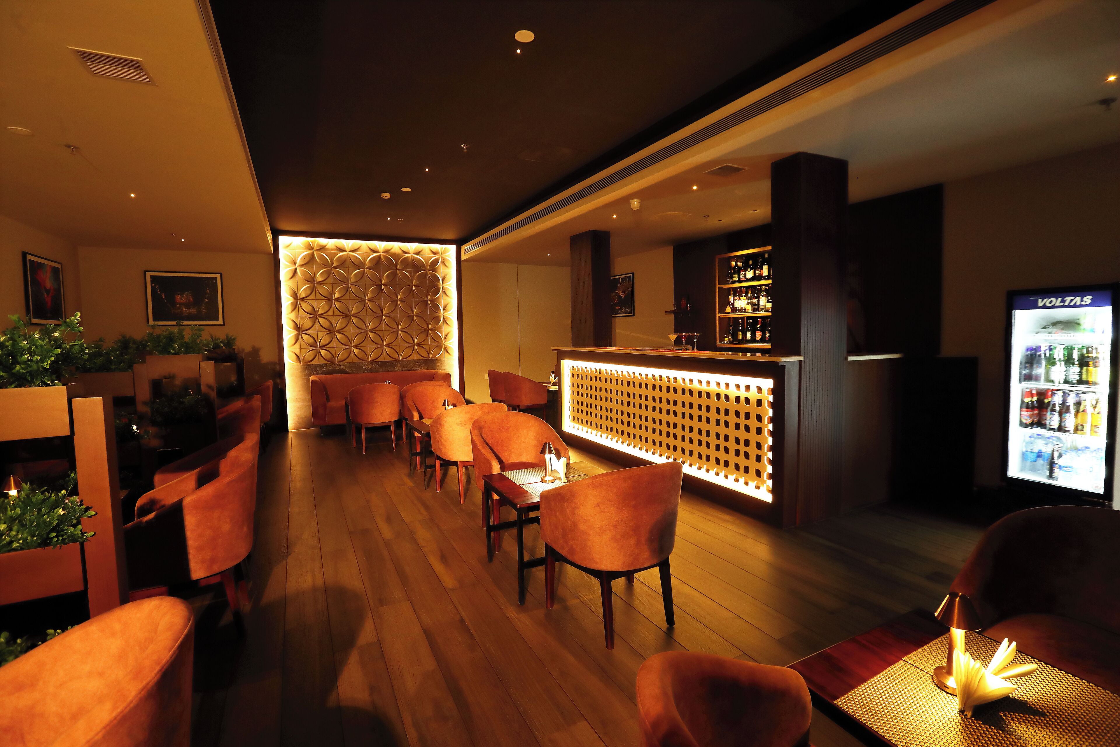 A bar area with wooden flooring, orange chairs, a bar counter, and a minibar.