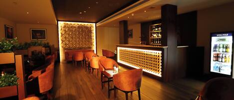 A bar area with wooden flooring, orange chairs, a bar counter, and a minibar.