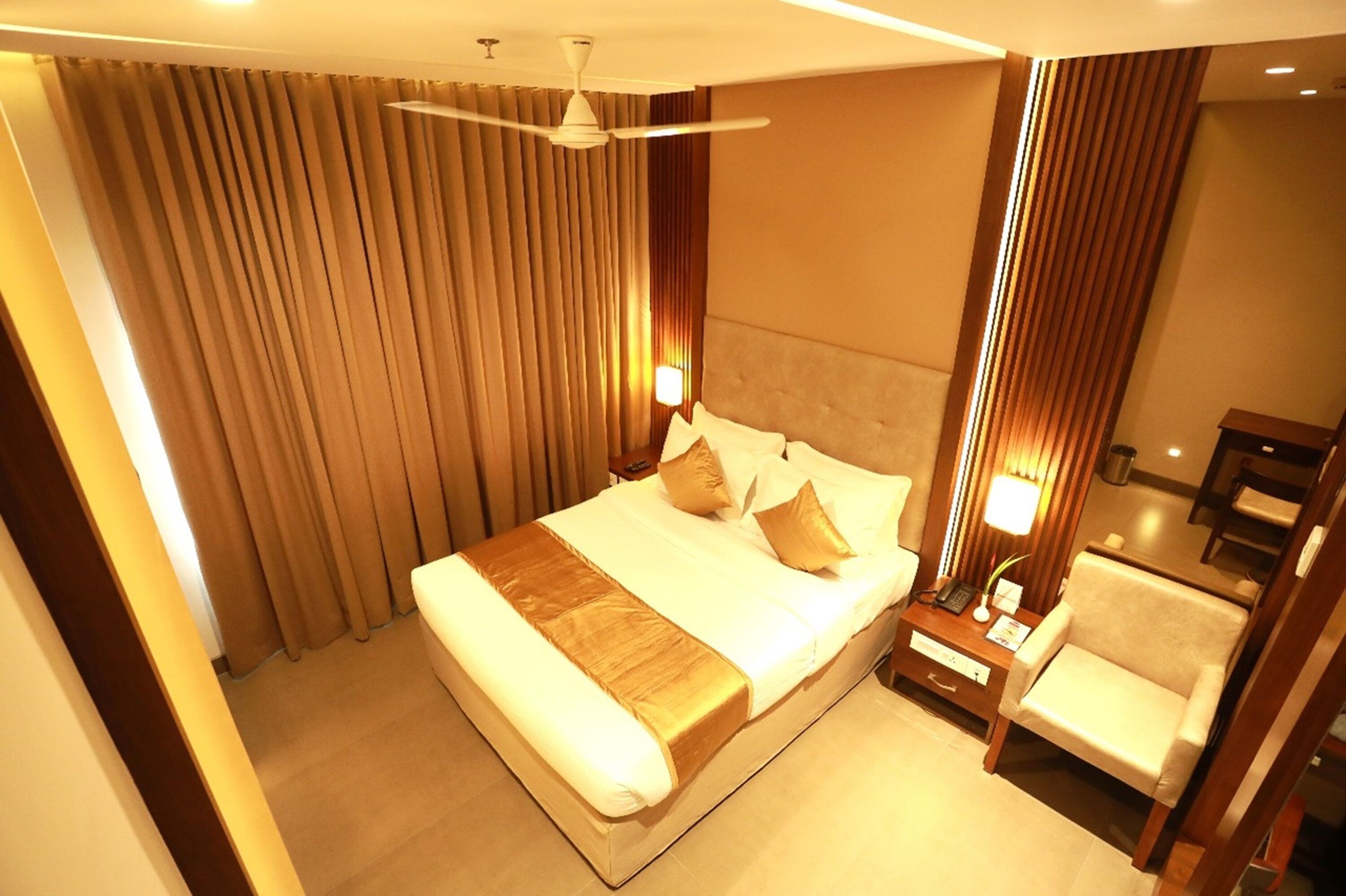 Une chambre d’hôtel avec un grand lit, un bureau avec une lampe, une chaise et un ventilateur de plafond.