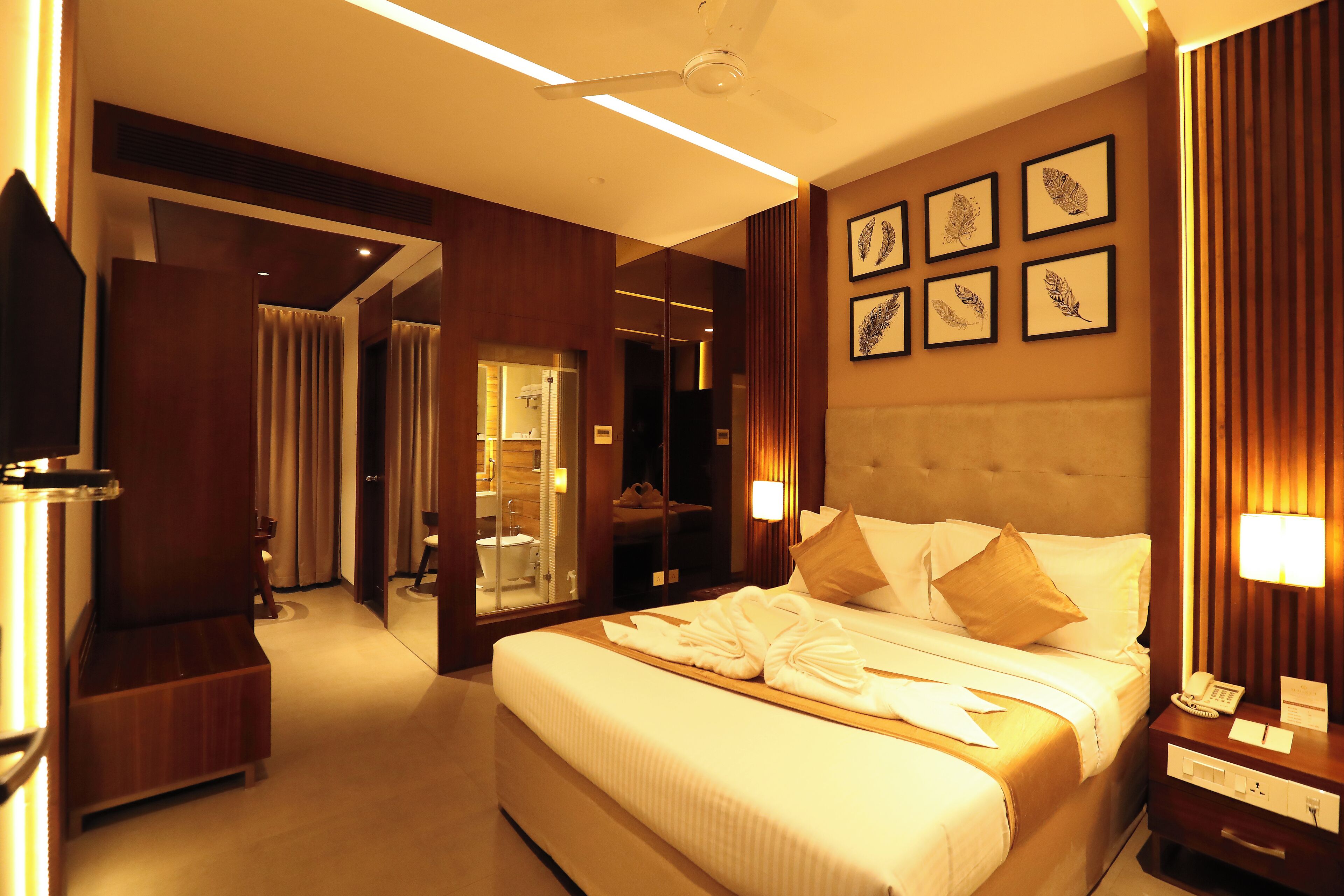 A hotel room with a large bed, a bedside table with a lamp, a mirror, and framed artwork on the wall.