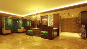 A modern reception area with a green wall, a reception desk, and a seating area with chairs. - Magnet Hotel (Kannur)