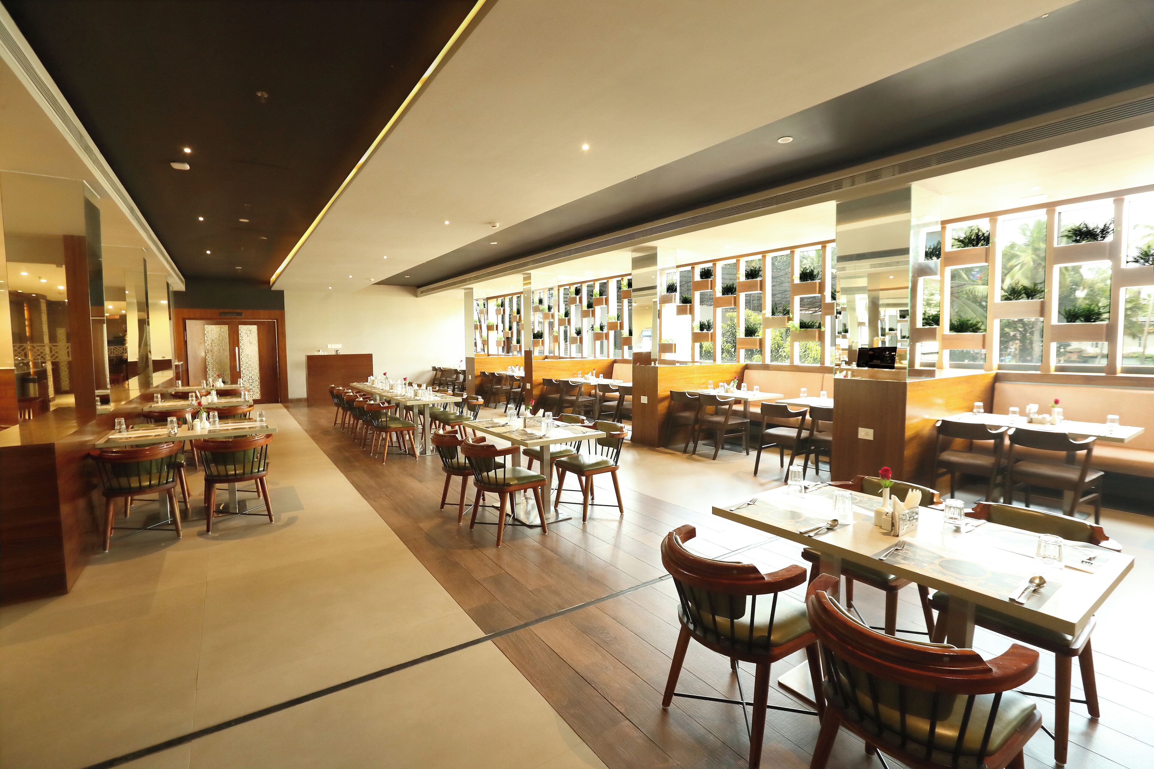 A spacious restaurant with multiple dining tables and chairs, a long counter, and a view of greenery through the windows.