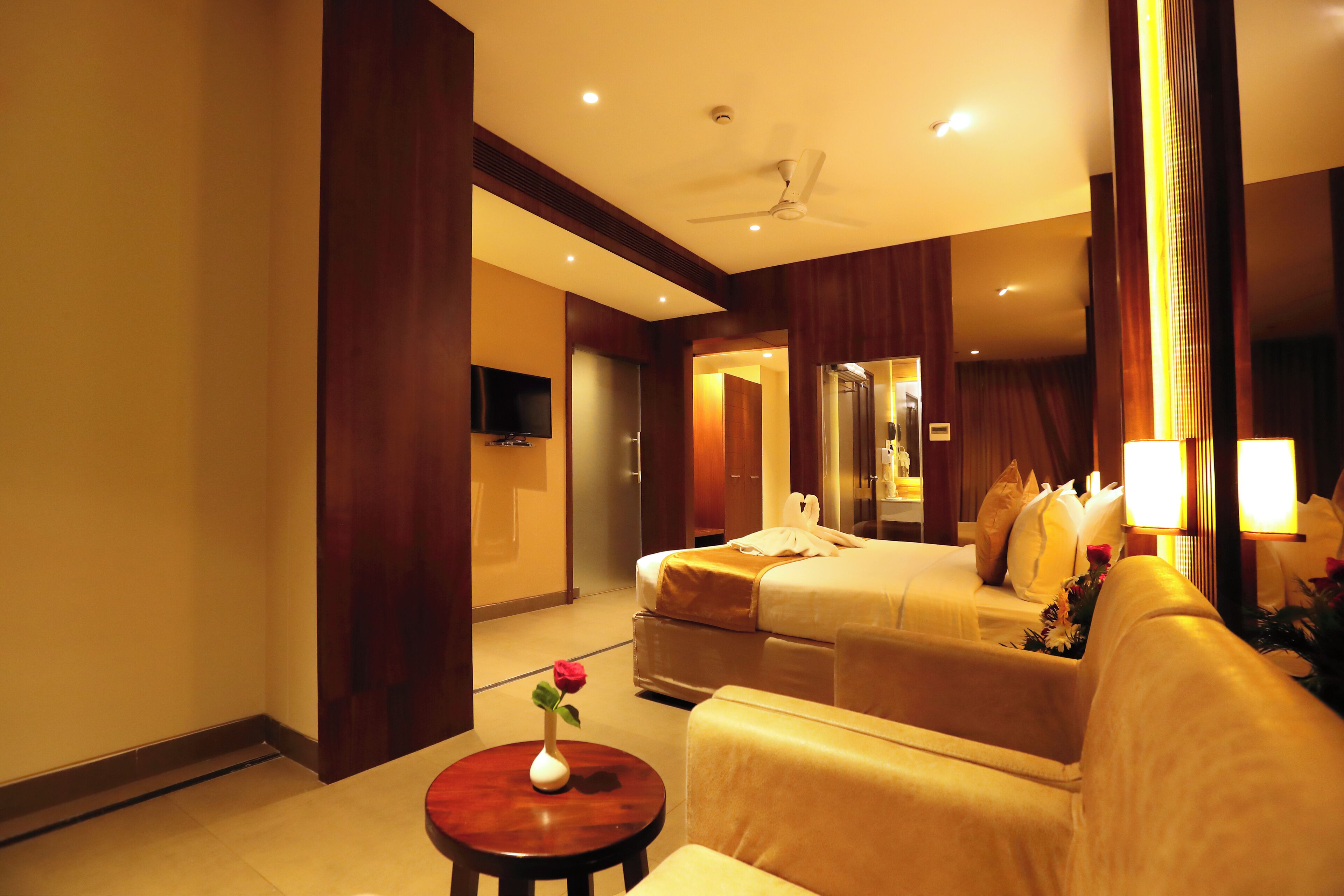 A hotel room with a bed, a sofa, a small table with a vase of flowers, and a television on the wall.
