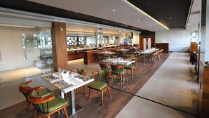 A modern restaurant with wooden flooring, green upholstered chairs, and neatly arranged tables with menus. - Magnet Hotel (Kannur)