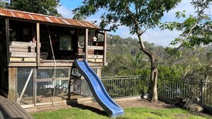 Ein hölzernes Spielhäuschen mit Rutsche, umgeben von einem eingezäunten Garten und Bäumen.