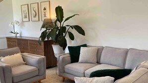 Ein Wohnzimmer mit grauem Sofa, zwei Sesseln, einem Couchtisch und einer großen Topfpflanze.