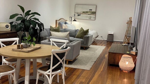 Ein modernes Wohnzimmer mit Essbereich, mit Holzboden, einem grauen Sofa, einem weißen Couchtisch und einer großen Topfpflanze.