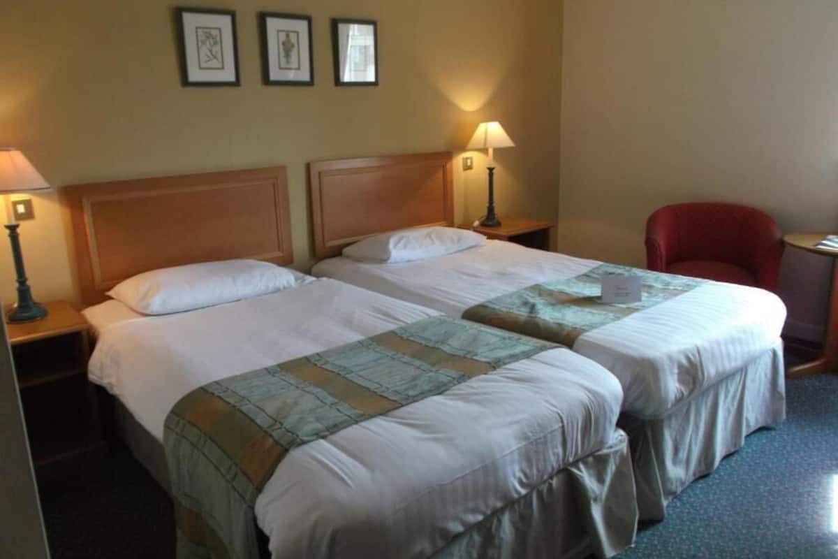A hotel room with two beds, a red chair, and a small table.