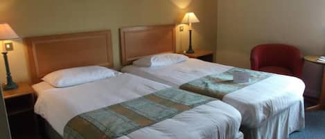 A hotel room with two beds, a red chair, and a small table.
