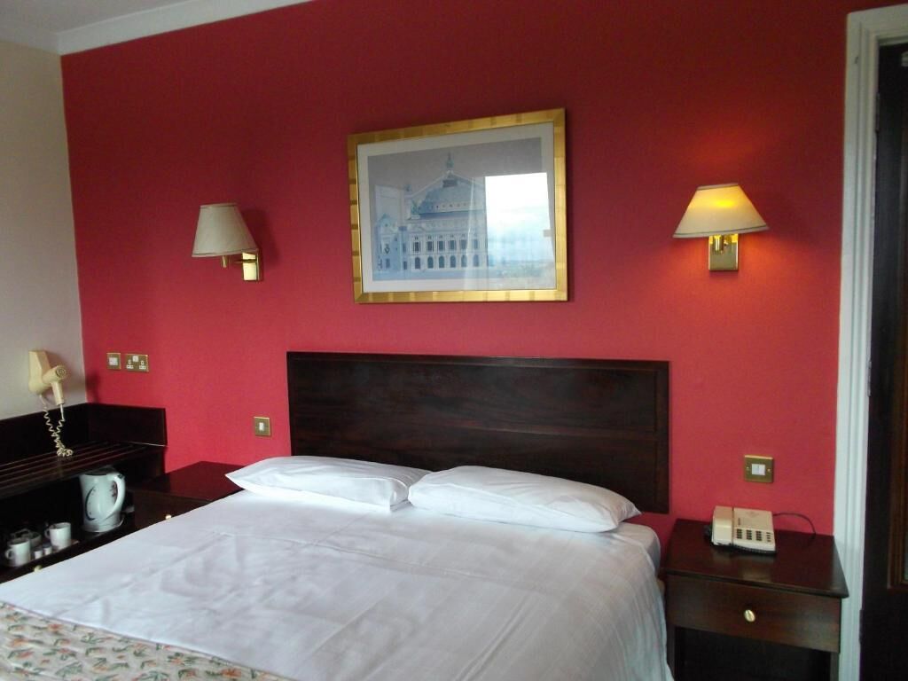 Una habitación de hotel con una cama grande, dos lámparas de noche, un cuadro en la pared y una mesita de noche con un teléfono.