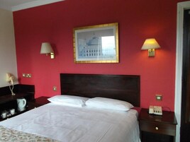 Ett hotellrum med en stor säng, två sänglampor, en inramad tavla på väggen och ett nattduksbord med en telefon.