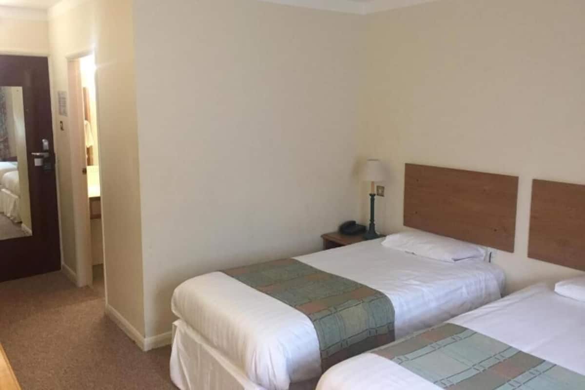 A hotel room with two beds, a nightstand with a lamp, and a door leading to another room.