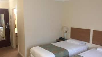 A hotel room with two beds, a nightstand with a lamp, and a door leading to another room.