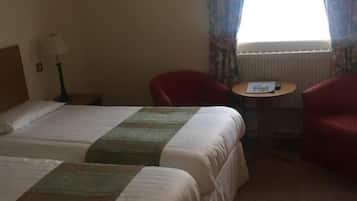 Una habitación de hotel con dos camas, una mesita, una silla y un ventanal con cortinas.