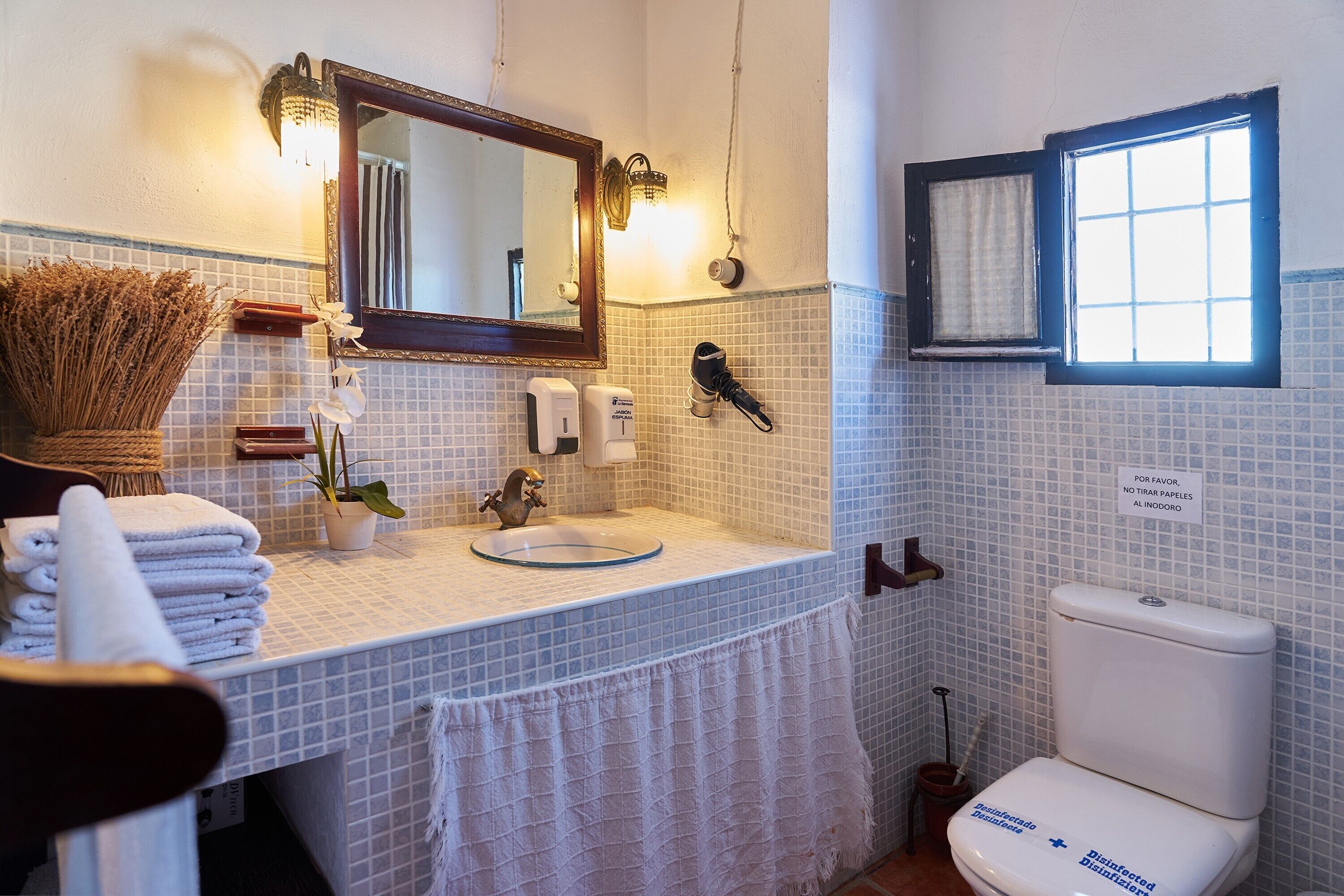 Un baño con lavamanos, espejo, pila de toallas y retrete.