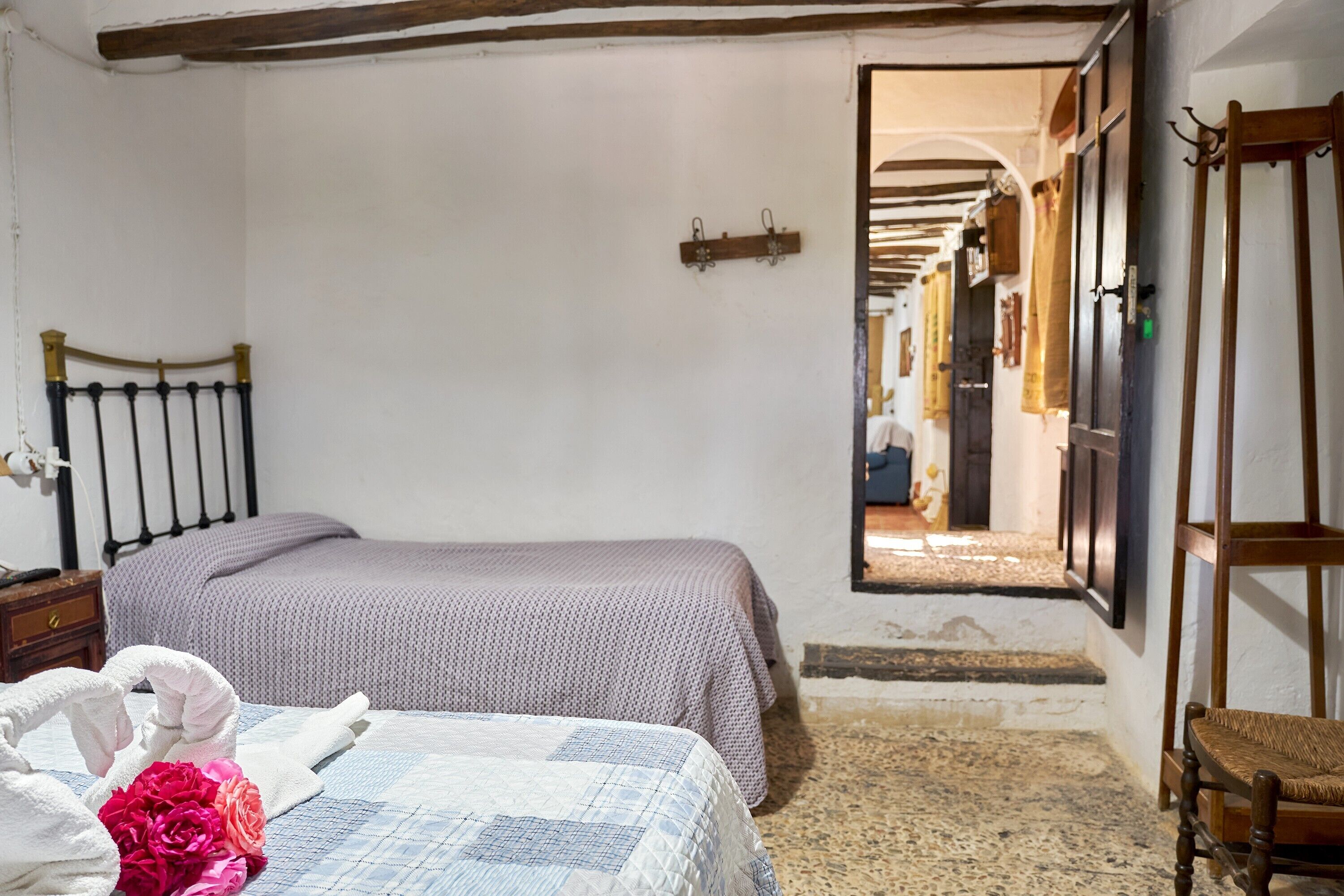 A bedroom with a bed, a nightstand, a chair, and a doorway leading to a corridor.