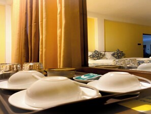 Habitación de hotel con cama, mesita de noche con una bandeja de vajilla blanca y un espejo que refleja la habitación.