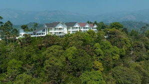 A large, multi-story hotel with a modern architectural style, surrounded by lush greenery and mountains in the background. - Sprise Munnar Resort and Spa (Devikolam)