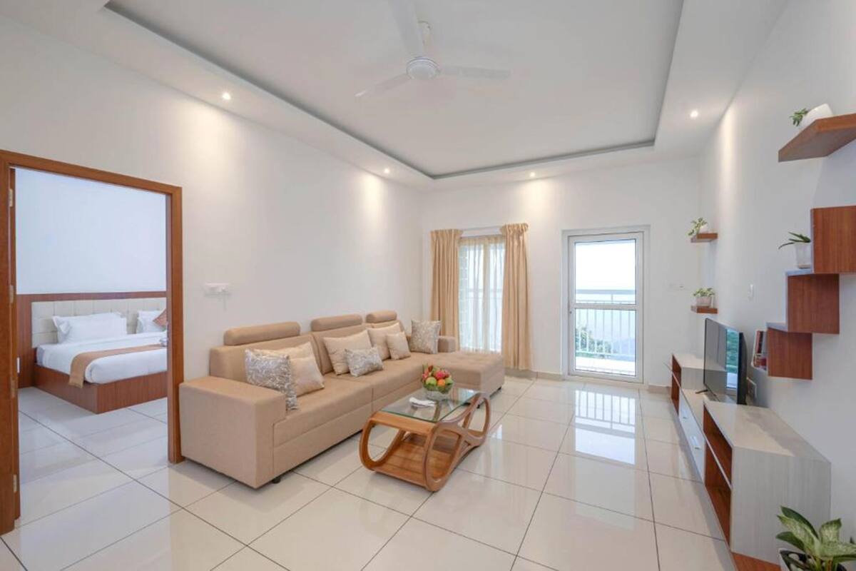 A modern living room with a sofa, a coffee table, a TV, and a balcony with curtains.