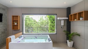 A modern bathroom with a large bathtub, a window with a view of trees, and wooden shelves with toiletries. - Sprise Munnar Resort and Spa (Devikolam)