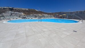 A swimming pool with a tiled deck, a lifeguard stand, and a view of buildings in the background.