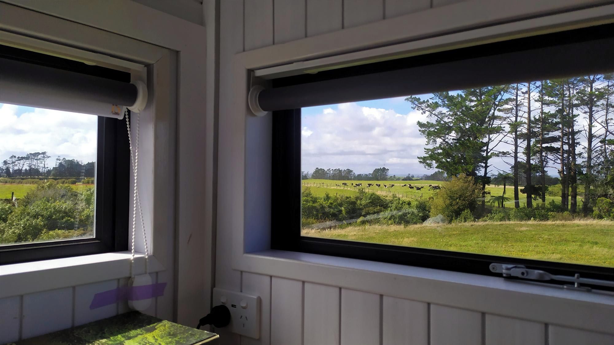 A room with two windows overlooking a rural landscape with fields and trees.